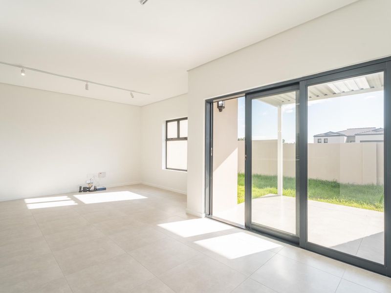 Bright and spacious open-plan living area featuring modern tiled flooring, track lighting, and large sliding glass doors leading to an outdoor patio.
