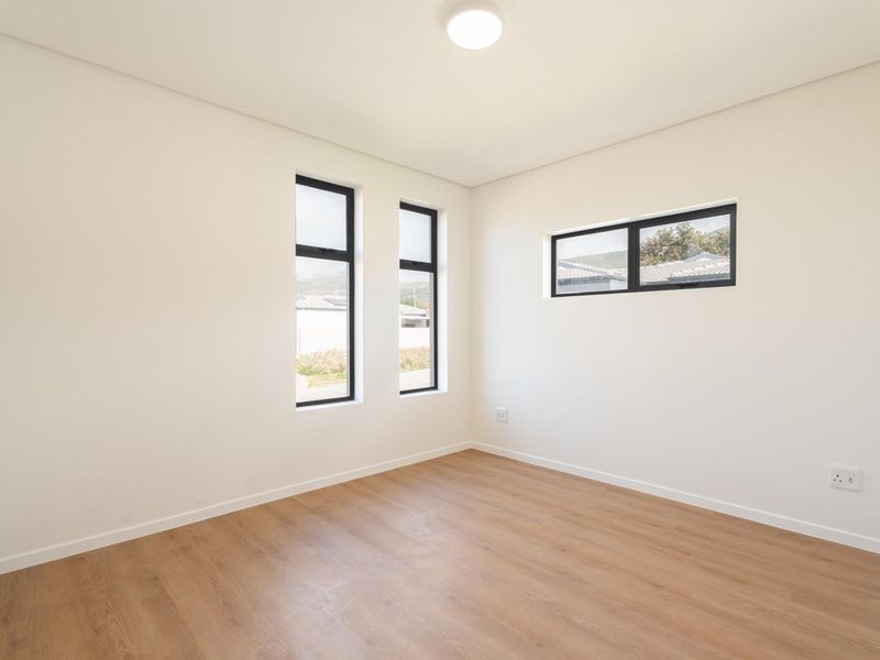A bright, modern, and empty bedroom featuring neutral walls, laminate flooring, and black-framed windows, offering a clean canvas for personalization.