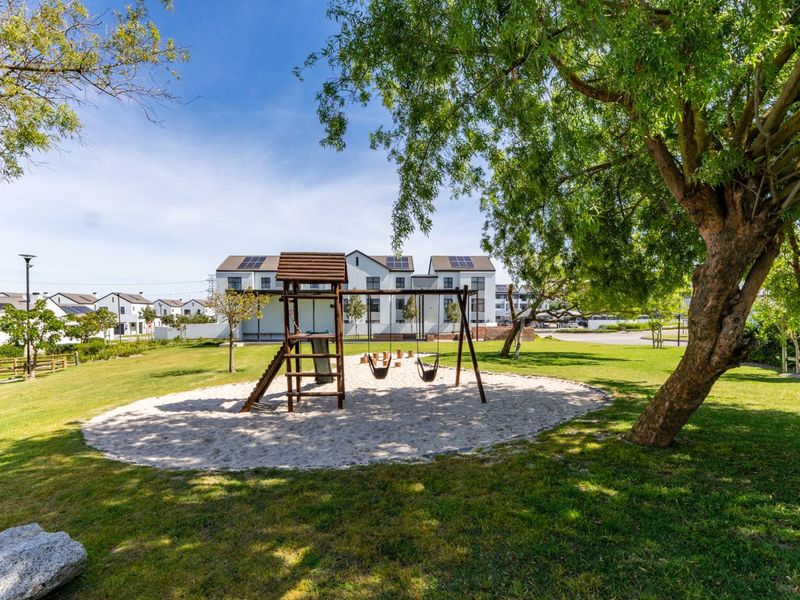 A well-maintained communal garden area featuring a children's playground with a sand pit, surrounded by landscaped lawns and mature trees.