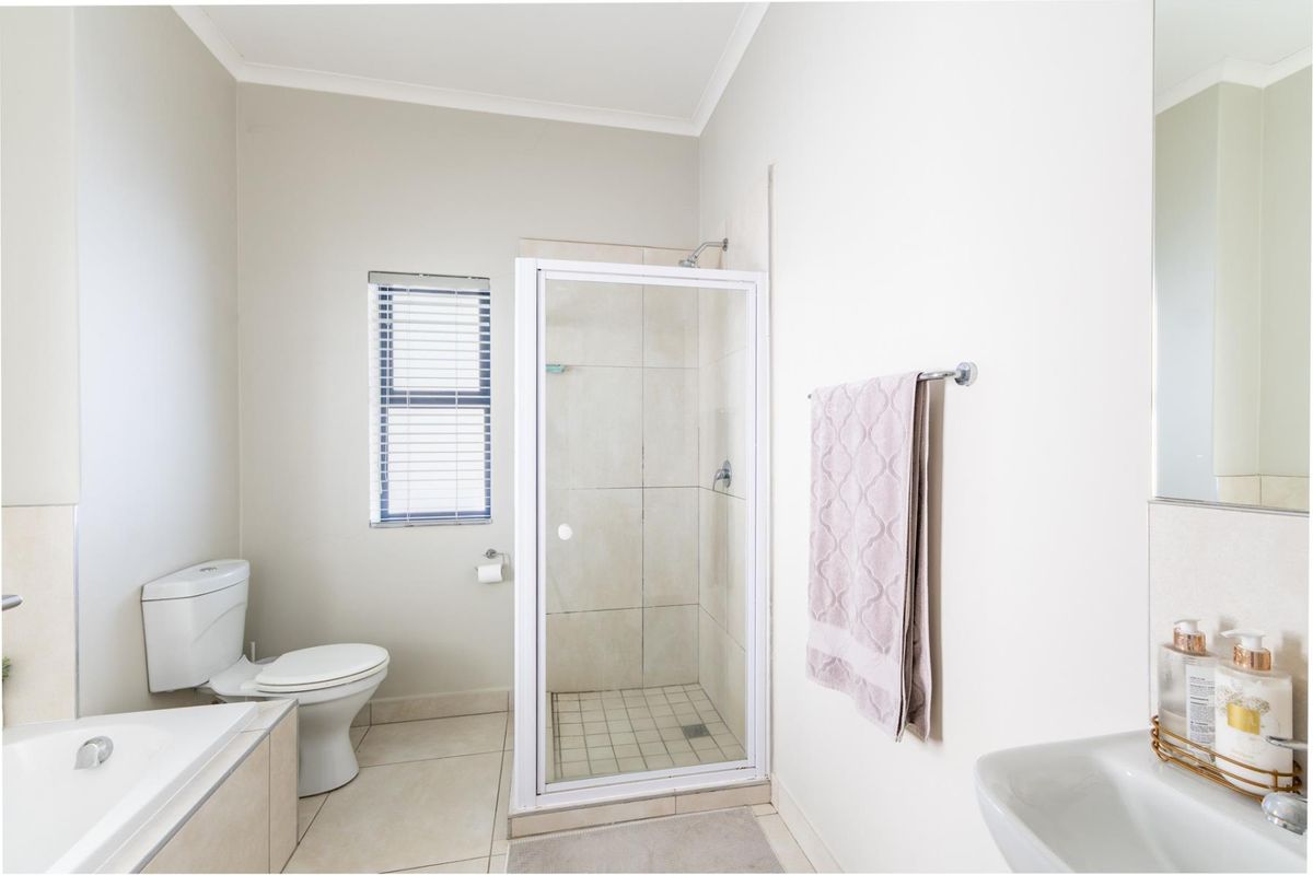 A clean and functional bathroom featuring a separate shower enclosure, bathtub, toilet, and a wall-mounted washbasin with neutral tiling.