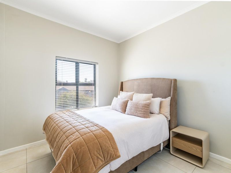 A well-maintained bedroom featuring neutral wall tones, tiled flooring, and a window fitted with venetian blinds.