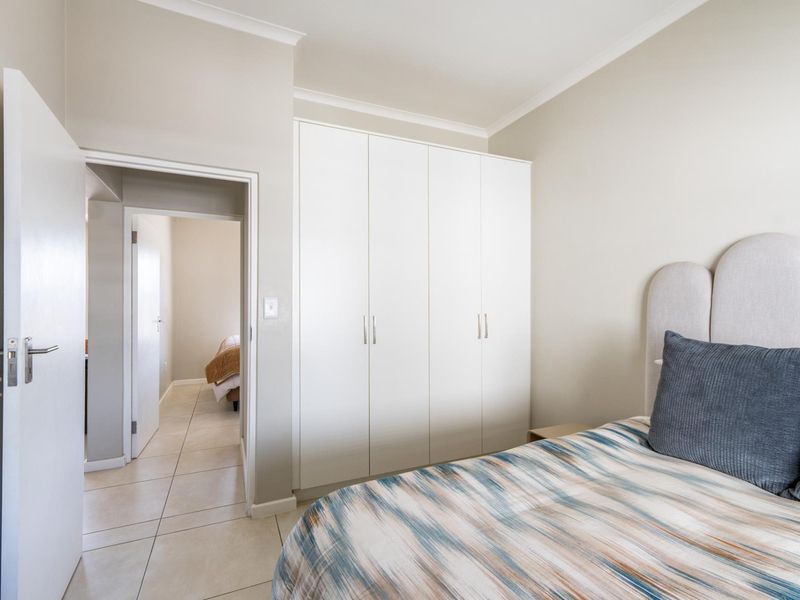 A well-maintained bedroom featuring neutral walls, tiled flooring, and a large built-in wardrobe with clean white finishes.