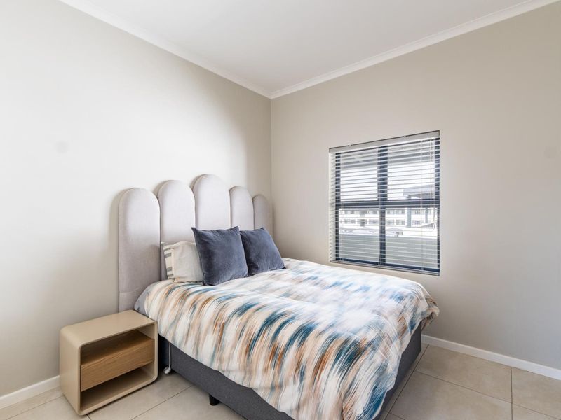 A well-maintained bedroom featuring neutral wall tones, tiled flooring, and a window fitted with venetian blinds.