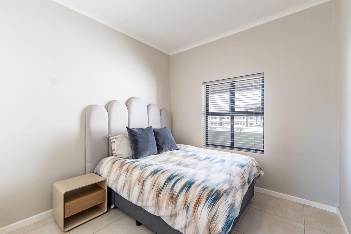 A well-maintained bedroom featuring neutral wall tones, tiled flooring, and a window fitted with venetian blinds.