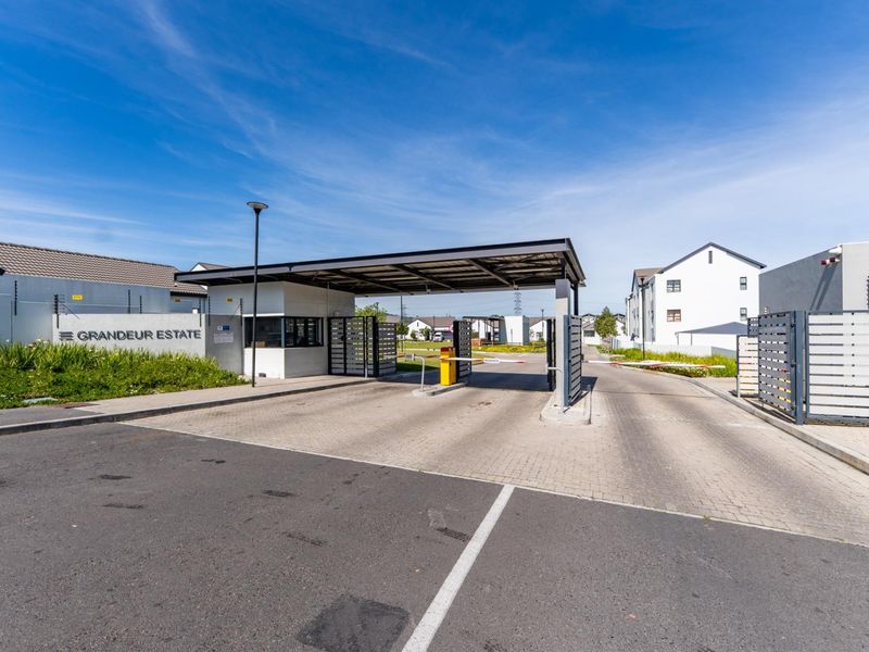 The secure entrance to Grandeur Estate featuring a manned gatehouse, boom gate access control, and perimeter electric fencing.