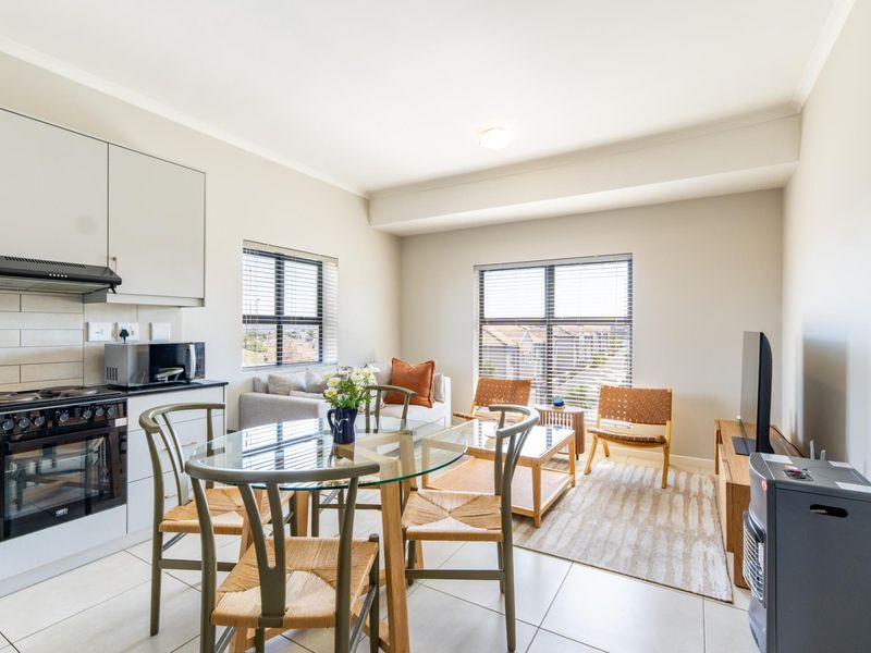 Open-plan living area featuring a modern kitchen with built-in appliances, tiled flooring, and large windows providing natural light.