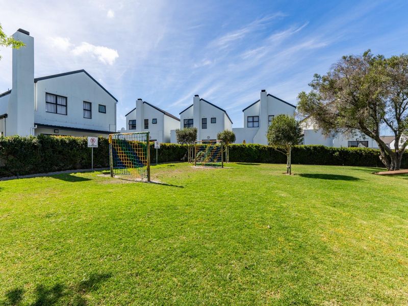 A well-maintained communal garden area featuring a manicured lawn, perimeter hedging, and a children's climbing frame set against a backdrop of residential units.
