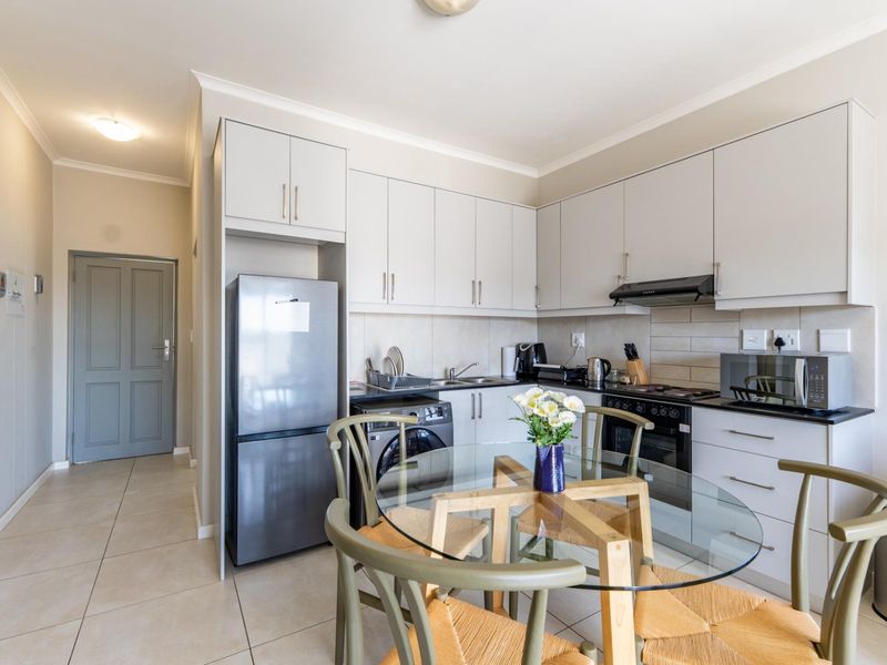 Modern open-plan kitchen featuring sleek cabinetry, integrated appliances, tiled backsplash, and durable floor tiles, seamlessly connecting to the dining area.