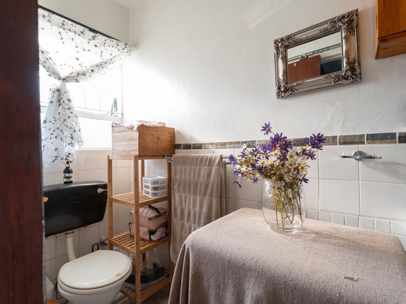 A compact bathroom featuring a wall-mounted basin, toilet, and tiled splashback, requiring cosmetic updates to modernize the space.