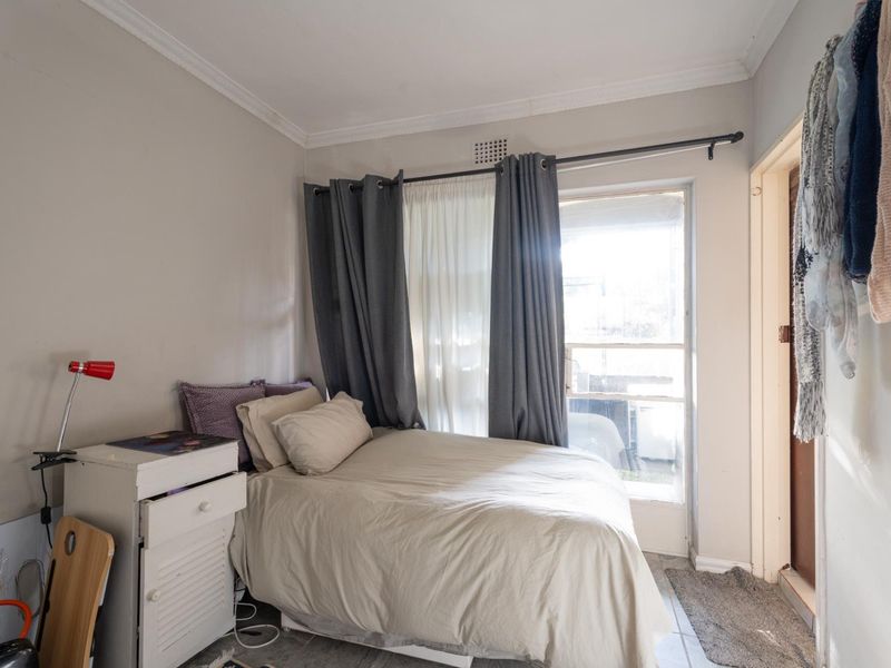 A compact bedroom featuring tiled flooring, crown molding, and a glass door providing natural light and access to an outdoor area.