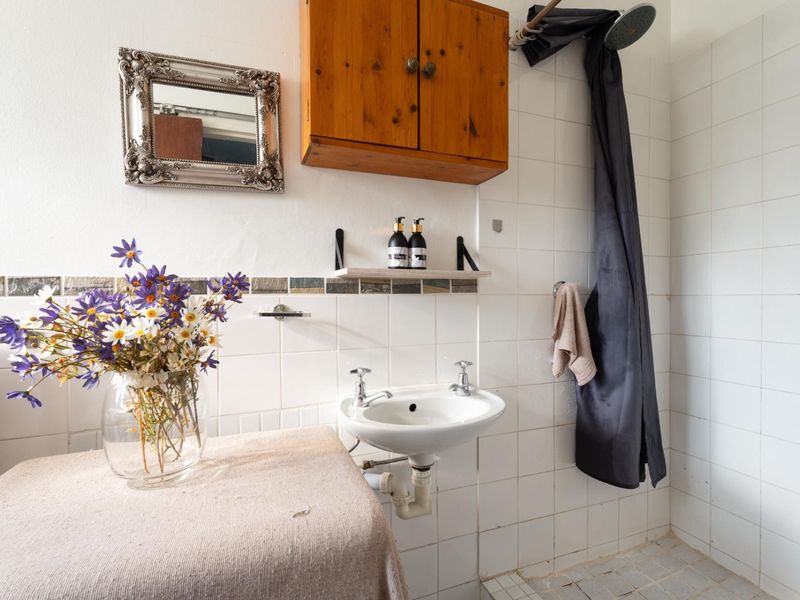 A functional bathroom featuring a wall-mounted basin, tiled shower area, and wooden storage cabinet, requiring some cosmetic updates to modernize the space.