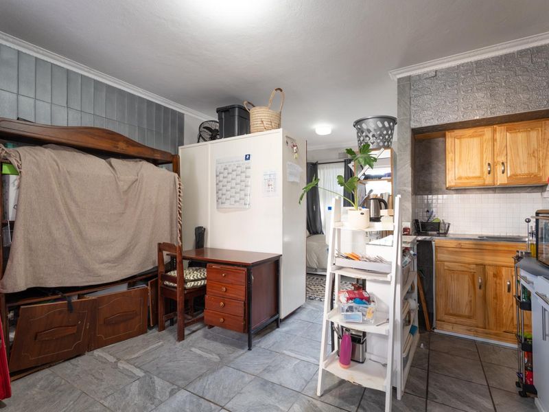 Open-plan living area featuring a compact kitchen with wooden cabinetry and tiled flooring, offering a functional layout for apartment living.