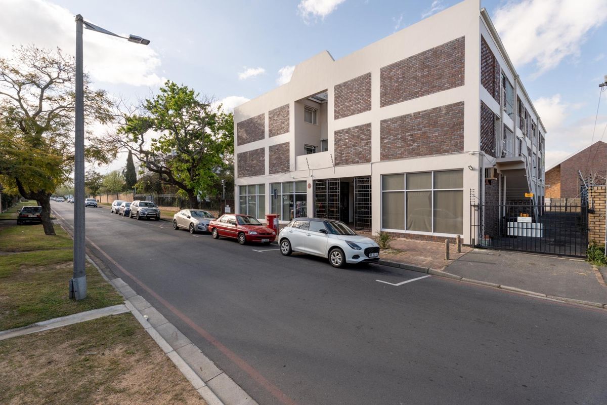 Street view of a multi-story apartment building featuring a brick and plaster facade, large windows, and perimeter security fencing.