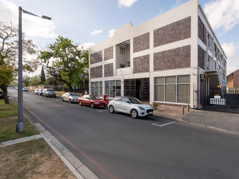 Street view of a multi-story apartment building featuring a brick and plaster facade, large windows, and perimeter security fencing.
