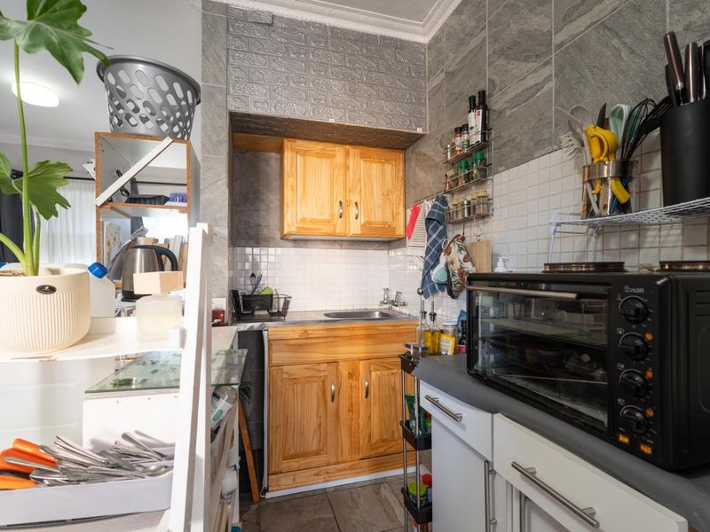 Compact kitchen area featuring wooden cabinetry, a stainless steel sink, and tiled backsplash with stone-effect wall accents.