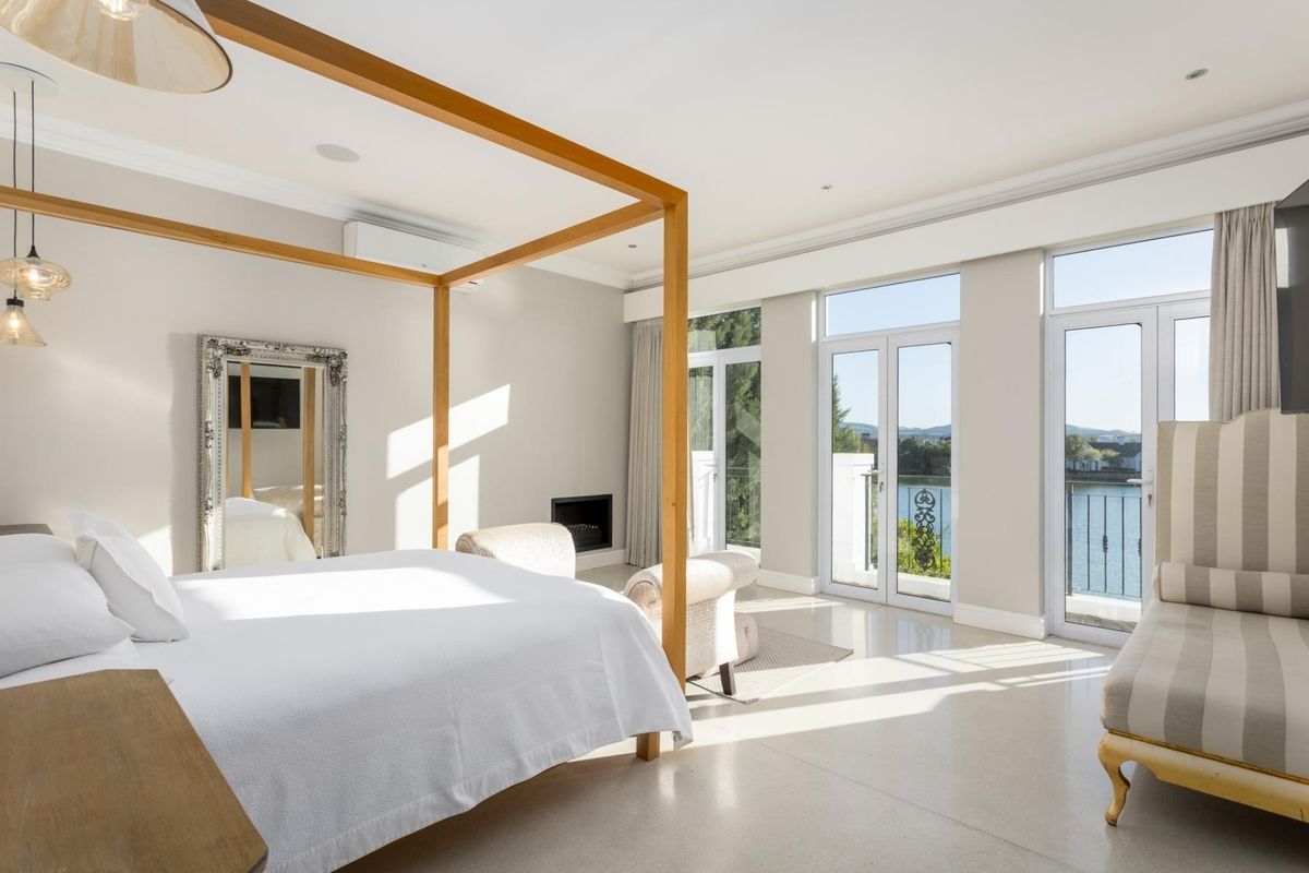 Spacious master bedroom featuring tiled floors, a built-in fireplace, split-system air conditioning, and large glass doors opening onto a private balcony with water views.