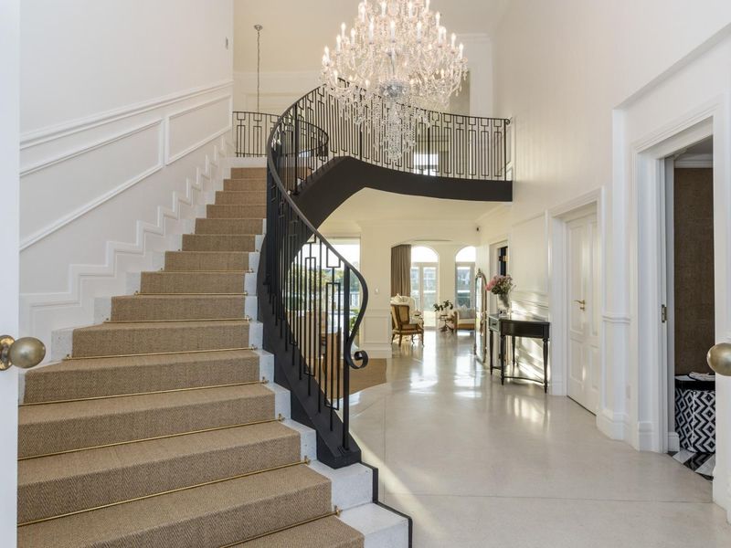 Grand entrance hall featuring a sweeping curved staircase with wrought iron balustrade, polished stone flooring, and an elegant crystal chandelier.