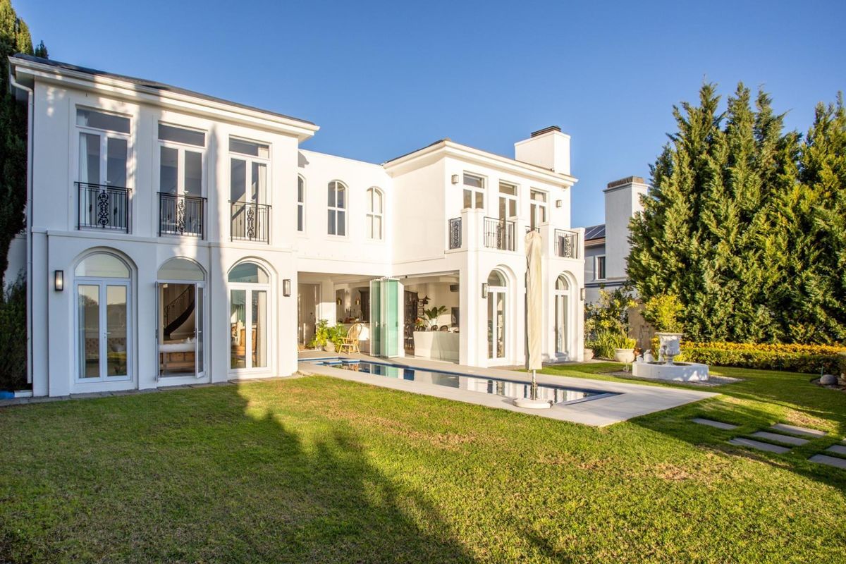 A beautifully maintained rear elevation of a luxury home featuring arched windows, balconies, and a sleek swimming pool set within a manicured garden.