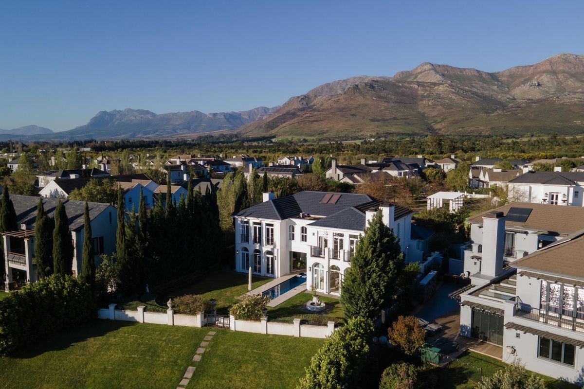 Aerial view of a luxury two-story residence featuring a swimming pool, landscaped garden, and mountain views in a secure estate setting.