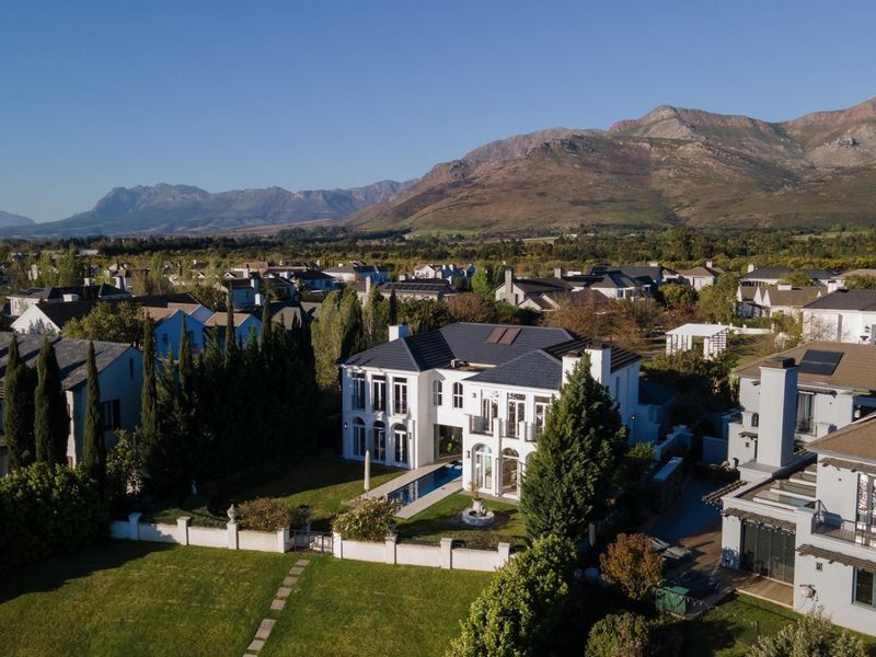 Aerial view of a luxury two-story residence featuring a swimming pool, landscaped garden, and mountain views in a secure estate setting.