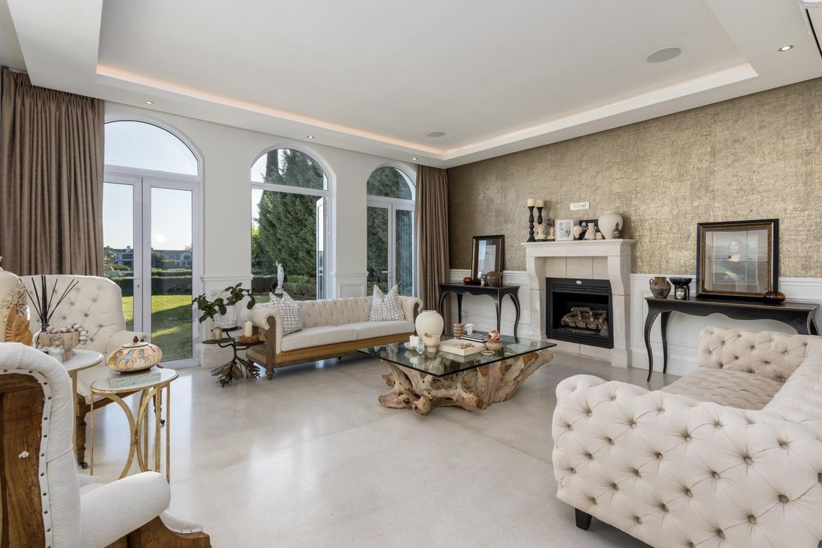 Elegant living room featuring a fireplace, stone flooring, recessed ceiling lighting, and large arched windows providing natural light and garden access.