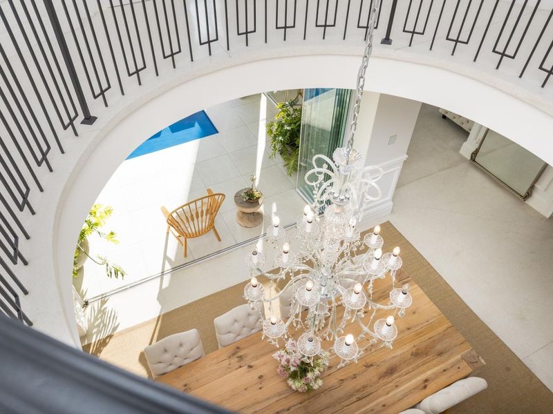 Elegant dining area featuring a grand crystal chandelier, curved staircase with wrought iron balustrade, and seamless access to the outdoor patio and pool area.