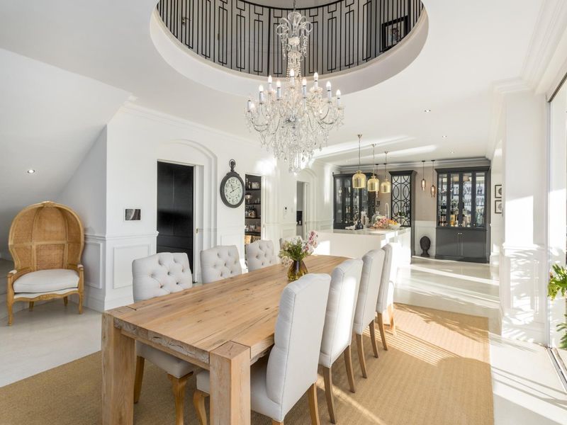 Elegant open-plan dining and kitchen area featuring a grand crystal chandelier, circular ceiling detail, and sophisticated built-in cabinetry with high-end finishes.
