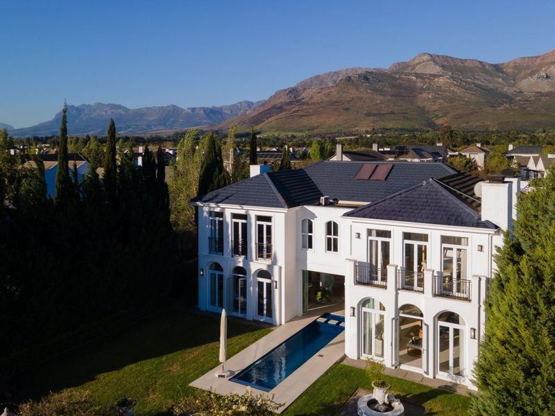 Aerial view of a luxury two-story residence featuring a swimming pool, manicured garden, and scenic mountain backdrop.