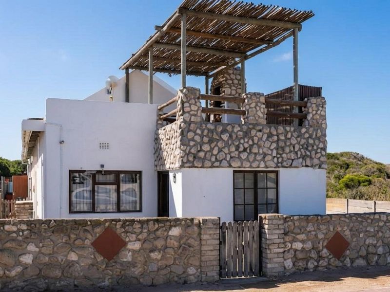 Front exterior view of a coastal-style house featuring stone cladding, a timber pergola, and a built-in outdoor braai area.