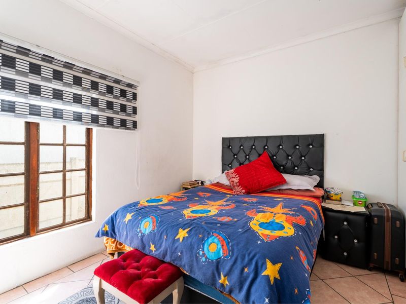 A functional bedroom featuring tiled flooring, a built-in wardrobe, and a timber-framed window, offering a neutral base for personalization.
