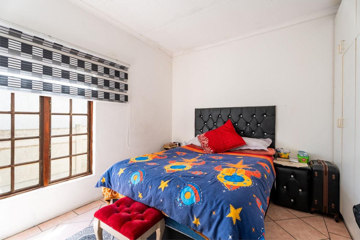 A functional bedroom featuring tiled flooring, a built-in wardrobe, and a timber-framed window, offering a neutral base for personalization.