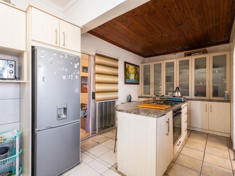 Functional kitchen featuring built-in cabinetry, a central island with a built-in oven and hob, tiled flooring, and a distinctive timber-paneled ceiling.
