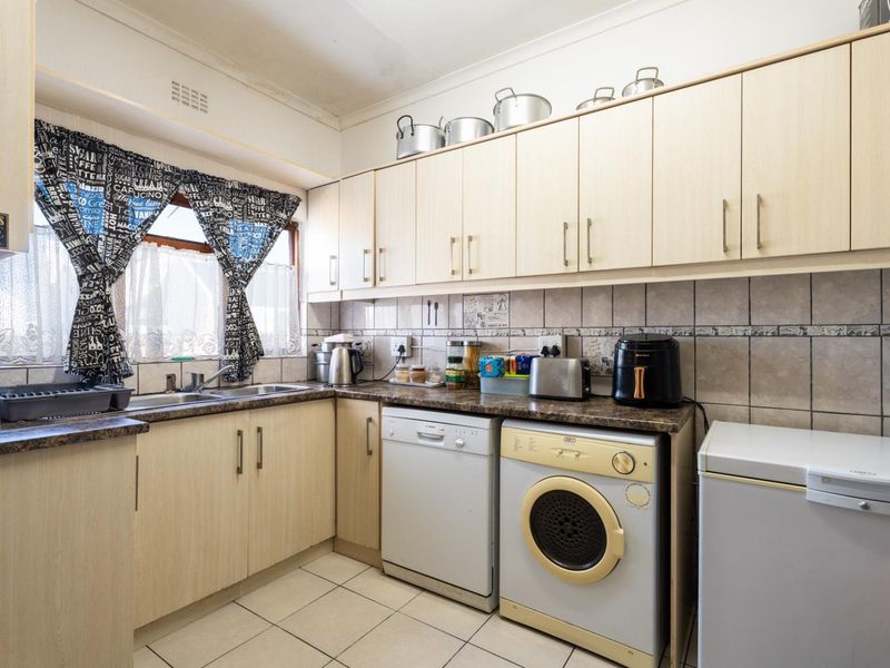 A functional kitchen featuring light-toned laminate cabinetry, tiled backsplash, and integrated laundry and dishwashing appliances.