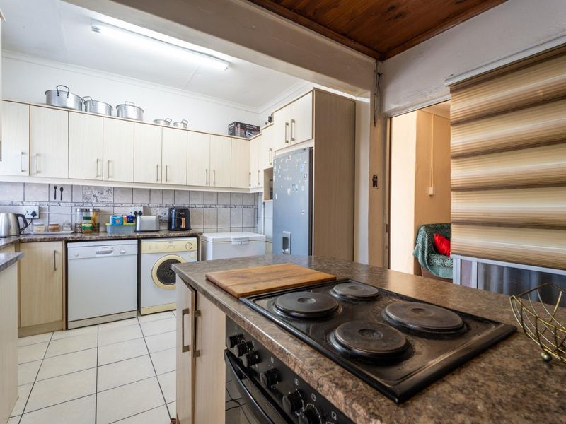 Functional kitchen featuring light-toned cabinetry, laminate countertops, an integrated electric hob and oven, tiled flooring, and a timber-paneled ceiling.