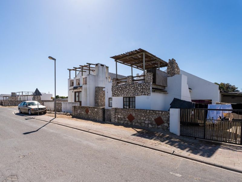 Front exterior view of a coastal-style house featuring stone cladding, a timber pergola, and a secure boundary wall.