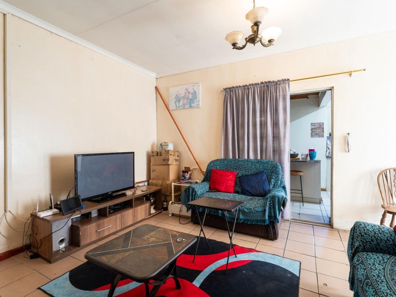 A living room featuring tiled flooring and a central light fixture, with direct access to an adjacent kitchen area.