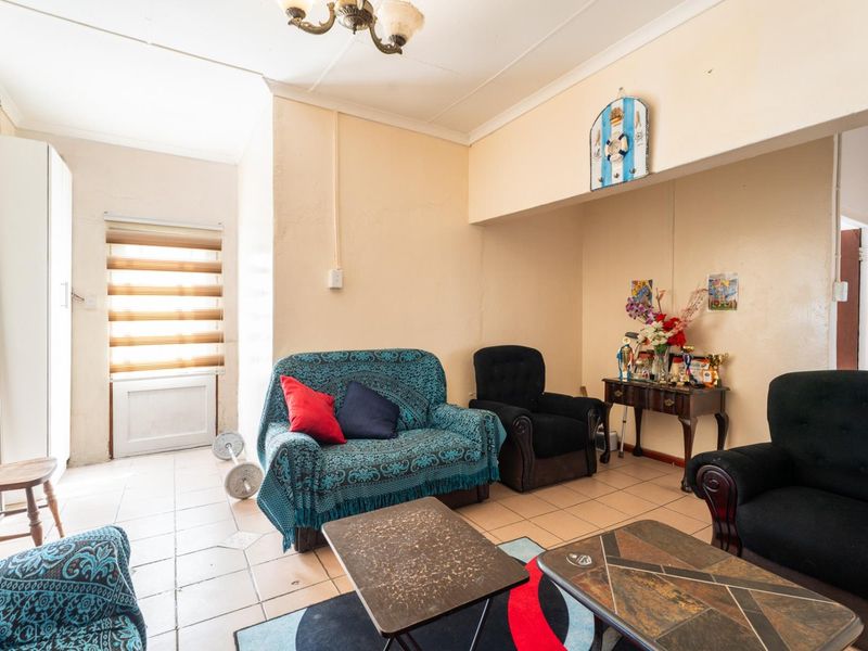 A living room area featuring tiled flooring and window blinds, offering a functional space with potential for cosmetic updates and modernization.
