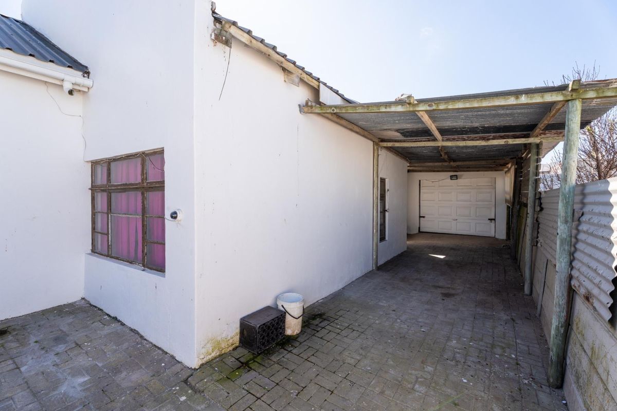 Rear exterior view showing a paved driveway, a covered carport area, and access to a garage with a white sectional door.