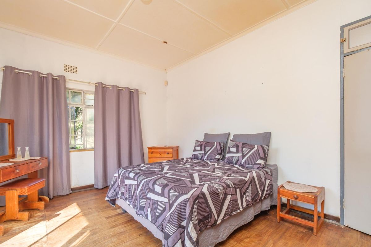 A bedroom featuring timber flooring and a ventilation brick, showing signs of wear and requiring cosmetic updates to the ceiling and finishes.