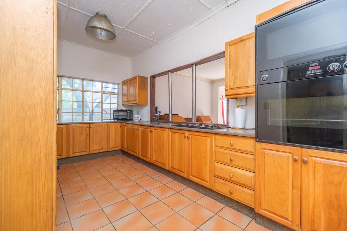 A dated kitchen featuring wooden cabinetry, built-in oven, hob, and tiled flooring, with a convenient pass-through window connecting to the adjacent living space.