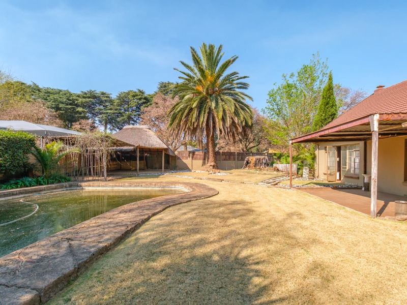Spacious rear garden featuring a swimming pool, covered patio with timber decking, and a traditional thatched lapa area.