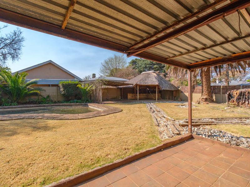 Covered patio overlooking a backyard featuring a swimming pool, a thatched lapa, and established garden space.