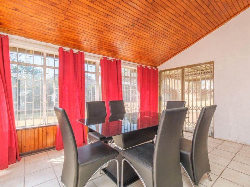 Dining area featuring a raked timber-clad ceiling, tiled flooring, and large windows with security bars, providing a bright and functional space.
