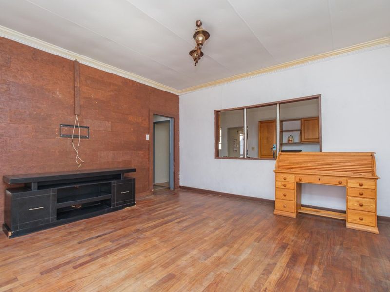 Living room featuring laminate flooring, a serving hatch to the kitchen, and a distinctive cork-clad feature wall.