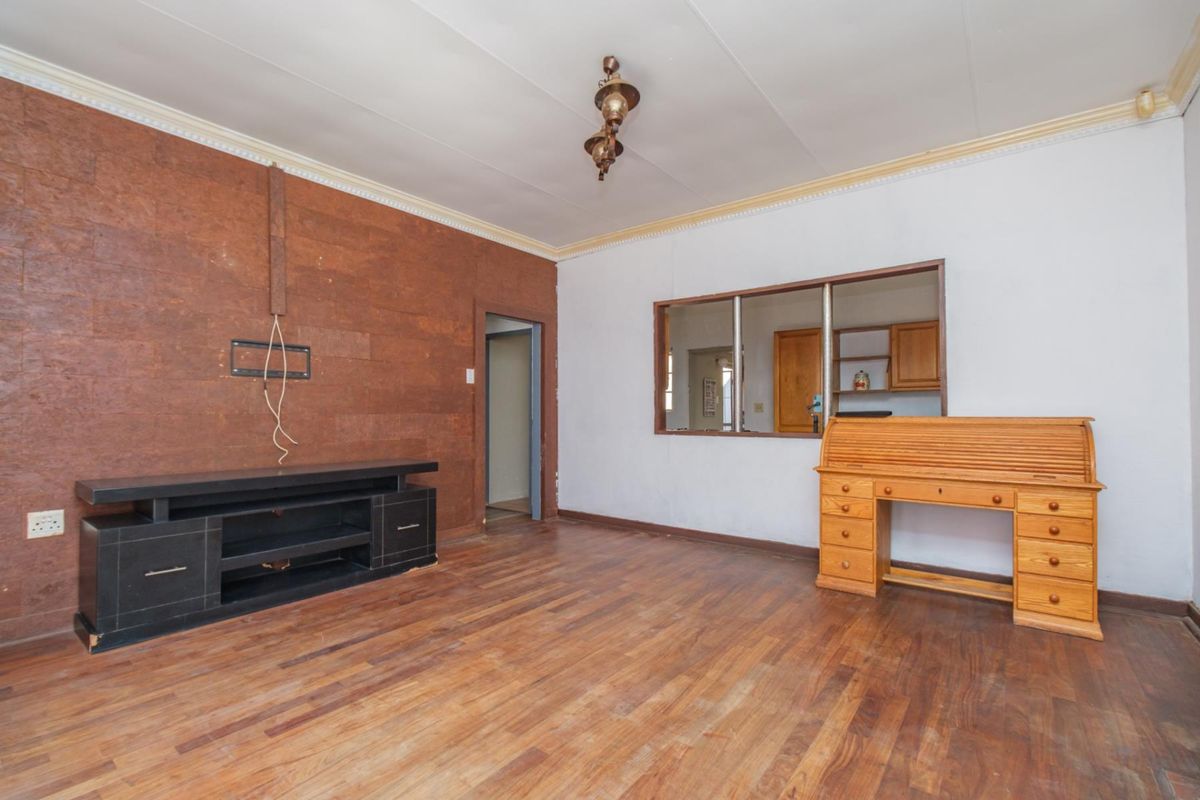 Living room featuring laminate flooring, a serving hatch to the kitchen, and a distinctive cork-clad feature wall.