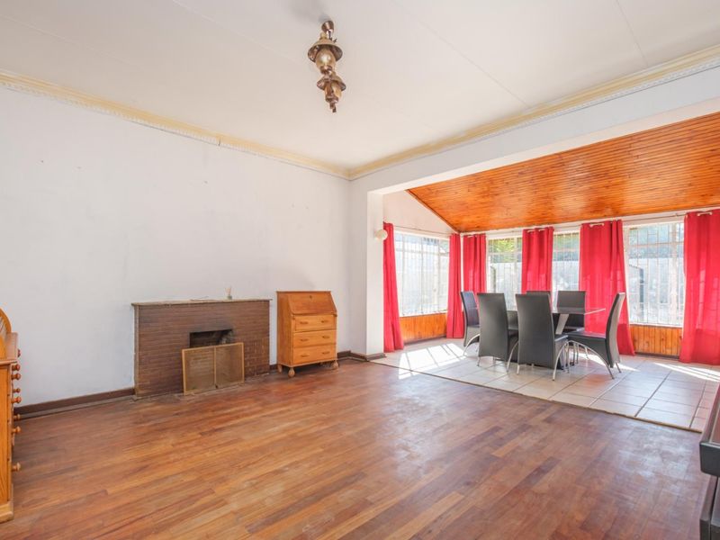 Spacious open-plan living and dining area featuring a brick fireplace, timber flooring, and a vaulted timber ceiling with large windows.
