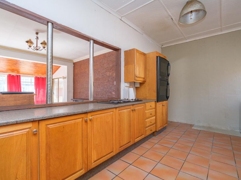 A dated kitchen featuring wooden cabinetry, built-in oven, hob, and tiled flooring, with a convenient pass-through window connecting to the adjacent living area.