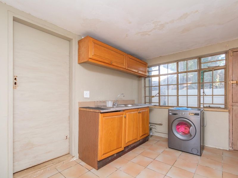 Laundry area featuring built-in wooden cabinetry, a stainless steel sink, tiled flooring, and steel-framed windows, requiring cosmetic updates.