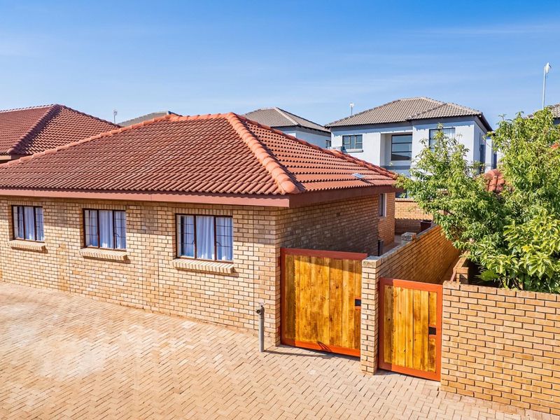 A well-maintained townhouse exterior featuring a face brick facade, tiled roof, and a secure paved driveway with a timber gate entrance.