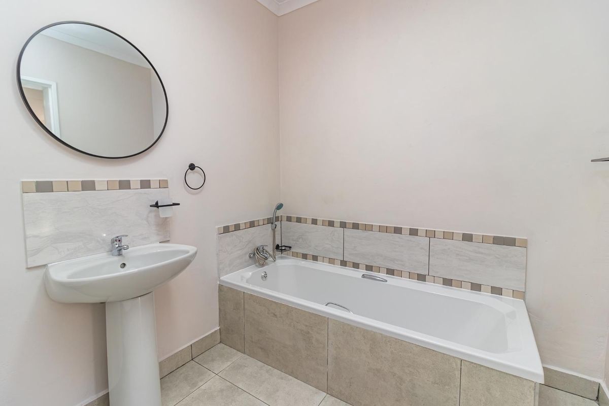 A clean and functional bathroom featuring a pedestal basin, a built-in bathtub with tiled surround, and neutral wall finishes.